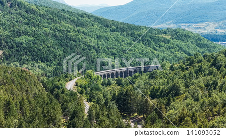 Train track viaduct spanning forested mountain valley Train track viaduct spanning forested mountain valley 141093052