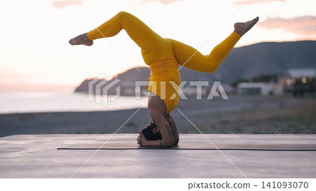 Woman practicing yoga headstand pose on beach at sunset 141093070