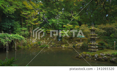 Kanazawa, Japan - Oct 6 2024, panoramic view of a pond surrounded by trees, with the Kaiseki Pagoda standing on the shore, in Kenroku-en Park, without people, at daytime, Kanazawa, Japan  141093320