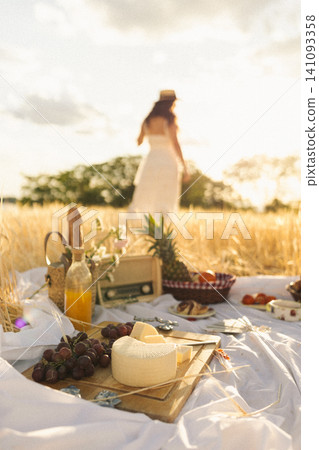 Woman enjoying a sunset picnic in a golden field Woman enjoying a sunset picnic in a golden field 141093358