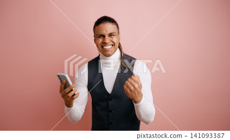 Latino man celebrating success holding smartphone Latino man celebrating success holding smartphone 141093387