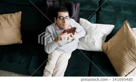 Person with spina bifida relaxing on a sofa reading Person with spina bifida relaxing on a sofa reading 141093480
