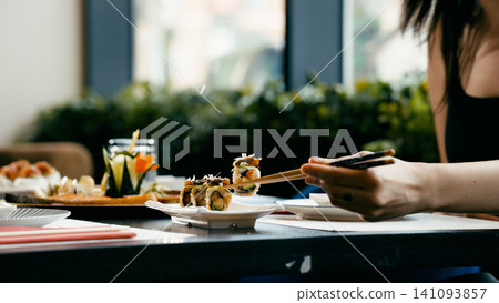 Woman enjoying sushi rolls with chopsticks at restaurant Woman enjoying sushi rolls with chopsticks at restaurant 141093857