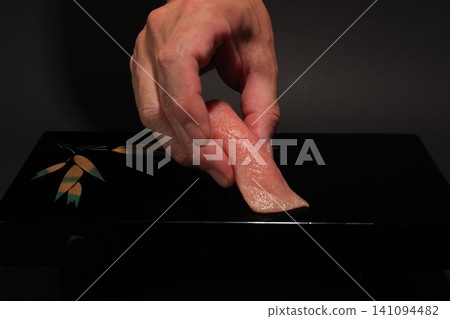 A scene where a sushi chef places fatty tuna nigiri sushi onto a black lacquered plate. A scene where a sushi chef places fatty tuna nigiri sushi onto a black lacquered plate. 141094482