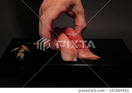 A scene where a sushi chef arranges medium fatty tuna and fatty tuna nigiri sushi on a black lacquered plate. A scene where a sushi chef arranges medium fatty tuna and fatty tuna nigiri sushi on a black lacquered plate. 141094483