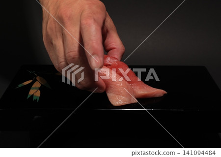 A scene where a sushi chef arranges medium fatty tuna and fatty tuna nigiri sushi on a black lacquered plate. A scene where a sushi chef arranges medium fatty tuna and fatty tuna nigiri sushi on a black lacquered plate. 141094484