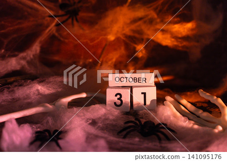 Dark still life composition featuring wooden block calendar displaying date 31 October Halloween holiday arrangement. Dramatic red lighting enhances mysterious atmosphere Dark still life composition featuring wooden block calendar displaying date 31 October Halloween holiday arrangement. Dramatic red lighting enhances mysterious atmosphere 141095176