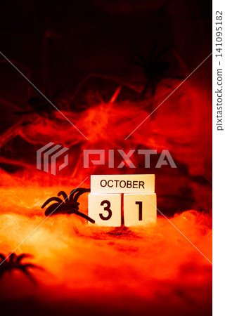 Dark still life composition featuring wooden block calendar displaying date 31 October Halloween holiday arrangement. Dramatic red lighting enhances mysterious atmosphere Dark still life composition featuring wooden block calendar displaying date 31 October Halloween holiday arrangement. Dramatic red lighting enhances mysterious atmosphere 141095182