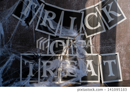 TRICK OR TREAT paper garland on decorative background of Halloween still life. Atmospheric Halloween concept designed for seasonal greetings classic spooky decorations to symbolize mystery TRICK OR TREAT paper garland on decorative background of Halloween still life. Atmospheric Halloween concept designed for seasonal greetings classic spooky decorations to symbolize mystery 141095183