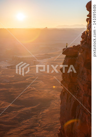 Majestic sunrise illuminates vast desert canyon landscape of Utah, USA, casting golden light across rugged terrain. lone person stands cliff edge, gazing with feeling of profound awe expansive Majestic sunrise illuminates vast desert canyon landscape of Utah, USA, casting golden light across rugged terrain. lone person stands cliff edge, gazing with feeling of profound awe expansive 141095686