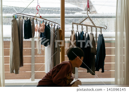 A scene depicting the daily life of an elementary school boy during winter break, including drying clothes indoors on a snowy day. 141096145