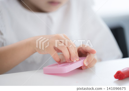 一個女孩專心致志地玩泥巴,培養創造力——寓教於樂、幼兒教育、治療和發展支持的畫面;沒有面孔。 一個女孩專心致志地玩泥巴,培養創造力——寓教於樂、幼兒教育、治療和發展支持的畫面;沒有面孔。 141096675