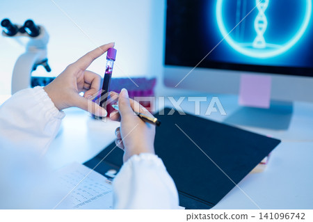 Laboratory Scientist Examining Blood Sample Test Tube with DNA Helix on Computer Screen Laboratory Scientist Examining Blood Sample Test Tube with DNA Helix on Computer Screen 141096742
