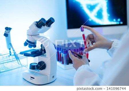 Laboratory Scientist Holding Blood Sample Test Tubes Near Microscope with DNA Screen Background Laboratory Scientist Holding Blood Sample Test Tubes Near Microscope with DNA Screen Background 141096744