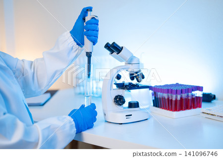 Scientist Using Pipette and Microscope in Medical Laboratory with Blood Sample Tubes 141096746