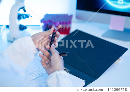Laboratory Technician Holding Blood Sample Test Tube with Clipboard and Microscope in Medical Lab Laboratory Technician Holding Blood Sample Test Tube with Clipboard and Microscope in Medical Lab 141096758