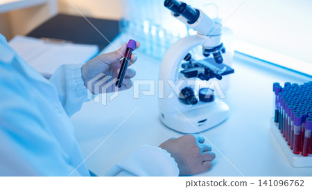 Laboratory Scientist Examining Blood Sample Test Tube Next to Microscope in Medical Research Lab Laboratory Scientist Examining Blood Sample Test Tube Next to Microscope in Medical Research Lab 141096762