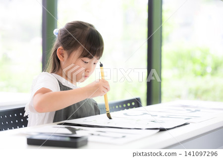 一位小學生正在專心練習書法,用毛筆書寫文字。學習書法的日本兒童表情嚴肅認真。 一位小學生正在專心練習書法,用毛筆書寫文字。學習書法的日本兒童表情嚴肅認真。 141097296