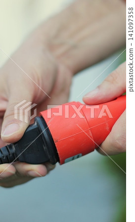 Vertical video Man plugs in an electric lawnmower. Close-up of a man hands plugging the cable into the outlet. Vertical video Man plugs in an electric lawnmower. Close-up of a man hands plugging the cable into the outlet. 141097358