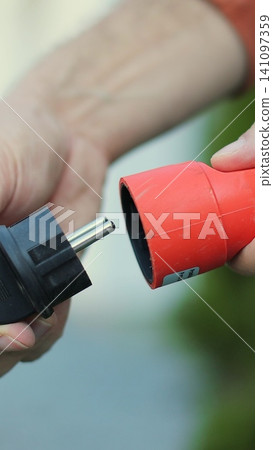 Vertical video Man plugs in an electric lawnmower. Close-up of a man hands plugging the cable into the outlet. Vertical video Man plugs in an electric lawnmower. Close-up of a man hands plugging the cable into the outlet. 141097359