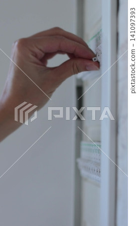 Vertical video Woman turns off the light on the electrical panel. Circuit breaker panel at home. Vertical video Woman turns off the light on the electrical panel. Circuit breaker panel at home. 141097393
