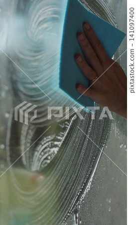 Vertical video Woman in rubber gloves sprays window cleaner from a spray bottle onto the windows glass. Housewife hands in rubber gloves cleaning windows close up. Cleaning glass window with a cloth Vertical video Woman in rubber gloves sprays window cleaner from a spray bottle onto the windows glass. Housewife hands in rubber gloves cleaning windows close up. Cleaning glass window with a cloth 141097400