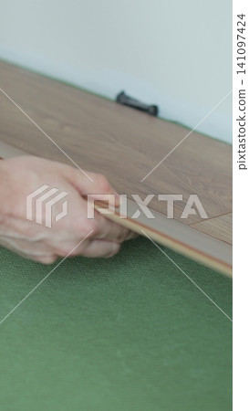 Vertical video Man lays laminate flooring on the floor in a room. Repair of the floor of the house. Vertical video Man lays laminate flooring on the floor in a room. Repair of the floor of the house. 141097424