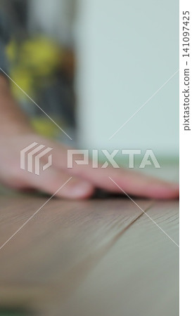 Vertical video Man kneeling and installing wood laminate floor in a home. Closeup on male hands. Vertical video Man kneeling and installing wood laminate floor in a home. Closeup on male hands. 141097425