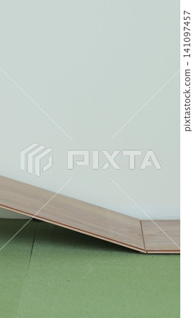 Vertical video Man kneeling and installing wood laminate floor in a home. Closeup on male hands. 141097457