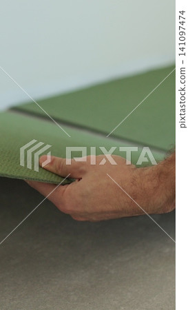 Vertical video Preparatory work before laying a laminate board. Man lays a noise-absorbing underlay under the laminate in advance. 141097474