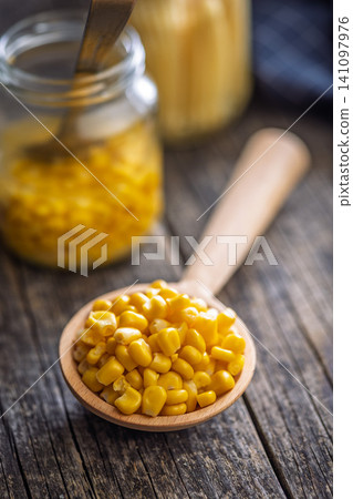 Canned Sweet Corn Kernels in a Wooden Spoon on Rustic Table With Blurred Jars Background 141097976