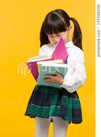 a frustrated young student in uniform holding books against a bright yellow background. a frustrated young student in uniform holding books against a bright yellow background. 141098200