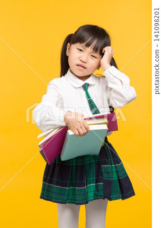 a confused schoolgirl scratching her head while holding textbooks against a yellow background. a confused schoolgirl scratching her head while holding textbooks against a yellow background. 141098201