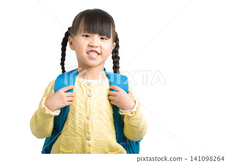 acheerful young schoolgirl wearing a blue backpack and smiling against a white background. acheerful young schoolgirl wearing a blue backpack and smiling against a white background. 141098264