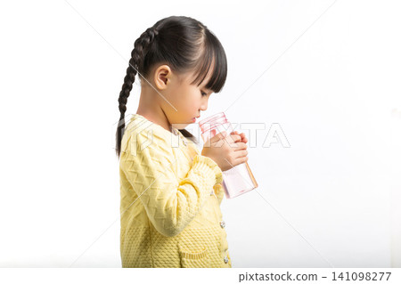 Side view of a cute young girl drinking water from a reusable pink sports bottle. 141098277
