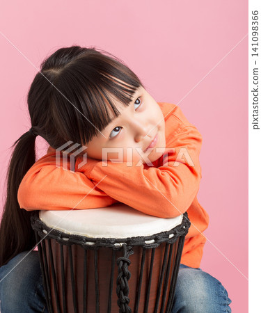 Cute Asian little girl playing drum, smiling child with percussion instrument on pink background, music education concept Cute Asian little girl playing drum, smiling child with percussion instrument on pink background, music education concept 141098366