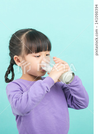 Little Asian girl drinking a glass of fresh milk for calcium and healthy growth, mint green background. Little Asian girl drinking a glass of fresh milk for calcium and healthy growth, mint green background. 141098394
