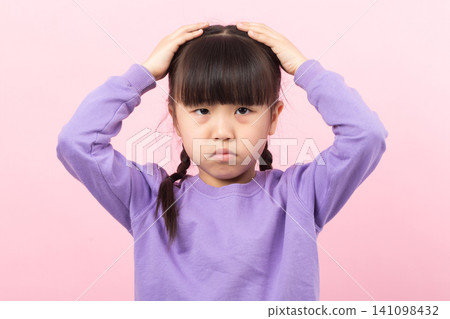An upset and moody little girl frowning while placing her hands on her head. An upset and moody little girl frowning while placing her hands on her head. 141098432