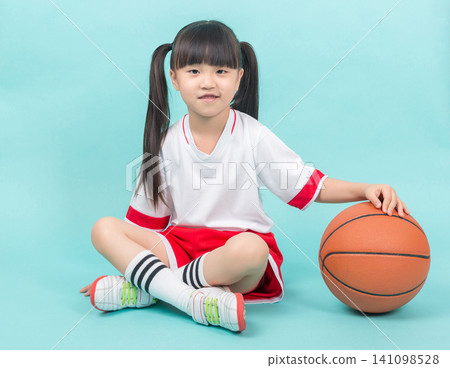 Studio backdrop: A little Asian girl sits on the floor holding a basketball, emphasizing children's sports and outdoor activities. Studio backdrop: A little Asian girl sits on the floor holding a basketball, emphasizing children's sports and outdoor activities. 141098528