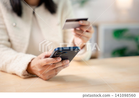 Business hand holding credit card and mobile phone for online payment, shopping during work at laptop computer as professional woman processes secure transaction on wooden desk 141098560
