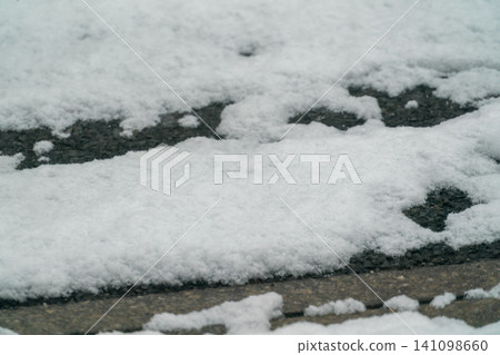 Close-up of a winter landscape: snow-covered asphalt roads and melting snow on the ground. Close-up of a winter landscape: snow-covered asphalt roads and melting snow on the ground. 141098660