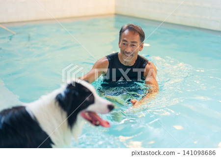 一位資深男性訓犬師和他的狗正在游泳池中進行復健訓練。 141098686