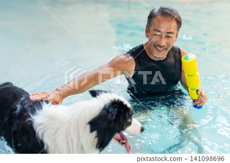 一位資深男性訓犬師和他的狗正在游泳池中進行復健訓練。 141098696