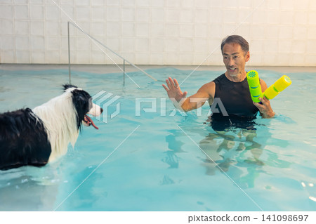 一位資深男性訓犬師和他的狗正在游泳池中進行復健訓練。 141098697