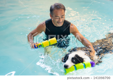 A senior male trainer and his dog undergoing rehabilitation in a swimming pool. A senior male trainer and his dog undergoing rehabilitation in a swimming pool. 141098700