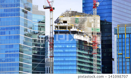 Crane on the construction site in a site surrounded by the high buildings. Office building under construction in the vicinity of high apartment buildings and office building. 141098707