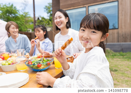 A three-generation family enjoying a barbecue in the garden. 141098778