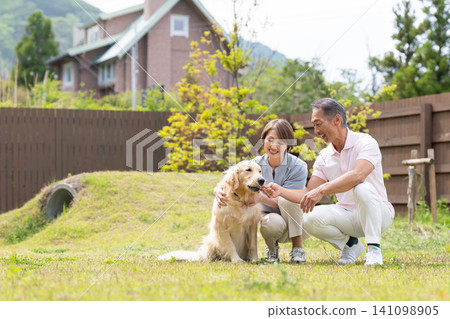 A smiling senior couple enjoying time with their golden retriever in the garden. A smiling senior couple enjoying time with their golden retriever in the garden. 141098905