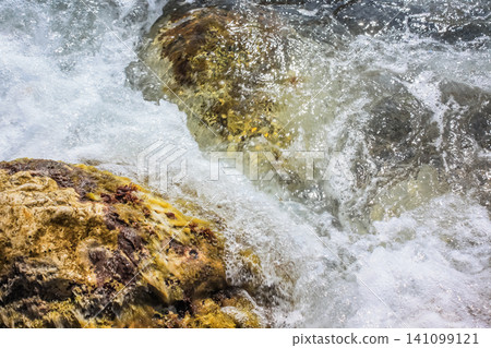 The waves breaking on a stony beach, forming a spray. Close up The waves breaking on a stony beach, forming a spray. Close up 141099121
