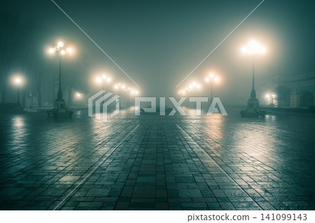 The main alley of a night winter park in a fog. Footpath in a fabulous winter city park at night in fog with benches and latterns. Beautiful foggy evening in the Mariinsky Park. Kyiv, Ukraine. The main alley of a night winter park in a fog. Footpath in a fabulous winter city park at night in fog with benches and latterns. Beautiful foggy evening in the Mariinsky Park. Kyiv, Ukraine. 141099143